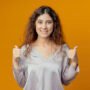 smiling young pretty girl her thumb up isolated on yellow background